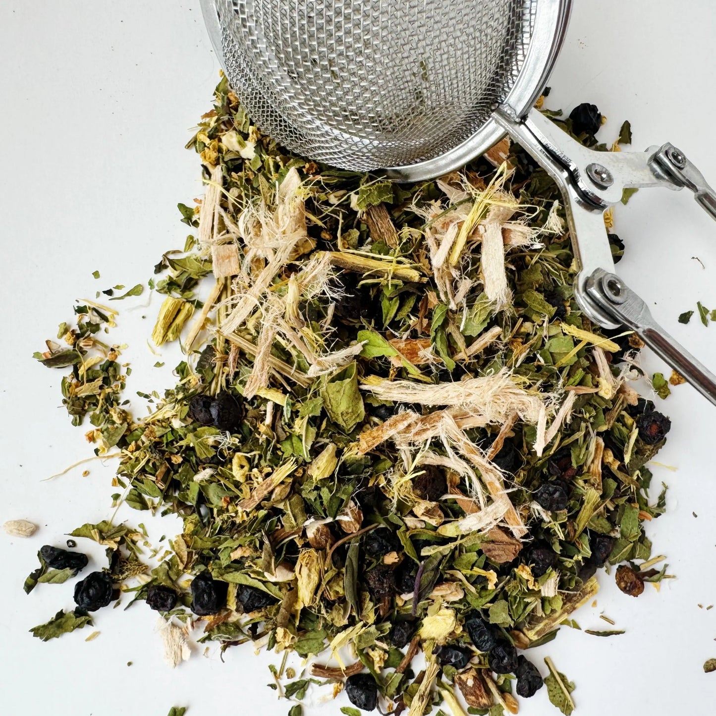 
This image shows a close-up of Passage Digestive Elixir Cirene loose-leaf tea, featuring a blend of dried herbs and botanicals in a white bowl with a tea infuser. Ingredients appear to include dried berries and various green leaves, ideal for digestive support.